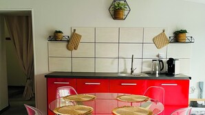 Cozinha moderna com armário vermelho, mesa de vidro e quatro cadeiras, e prateleira hexagonal com planta.