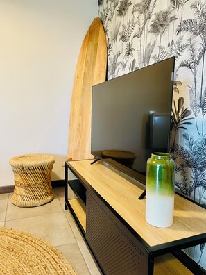 Ein modernes Wohnzimmer mit einem Flachbildfernseher auf einem Holzbodenständer, einem gewebten Hocker und einer grünen Vase auf dem Boden.
