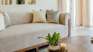 Uma sala de estar moderna com um sofá bege, uma mesa de centro com uma planta e uma vela, e estantes embutidas com objetos decorativos.