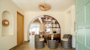 Um hall com balcão de recepção, duas cadeiras de vime, uma grande porta em arco e um lustre.