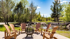 Eine Terrasse mit Adirondack-Stühlen, einem Feuerkorb und Blick auf einen Teich.