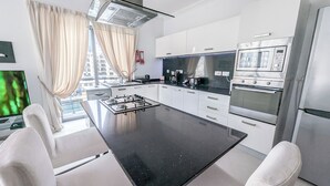 Una cucina moderna con isola centrale, mobili bianchi, elettrodomestici in acciaio inossidabile e vista sulla città attraverso ampie finestre.