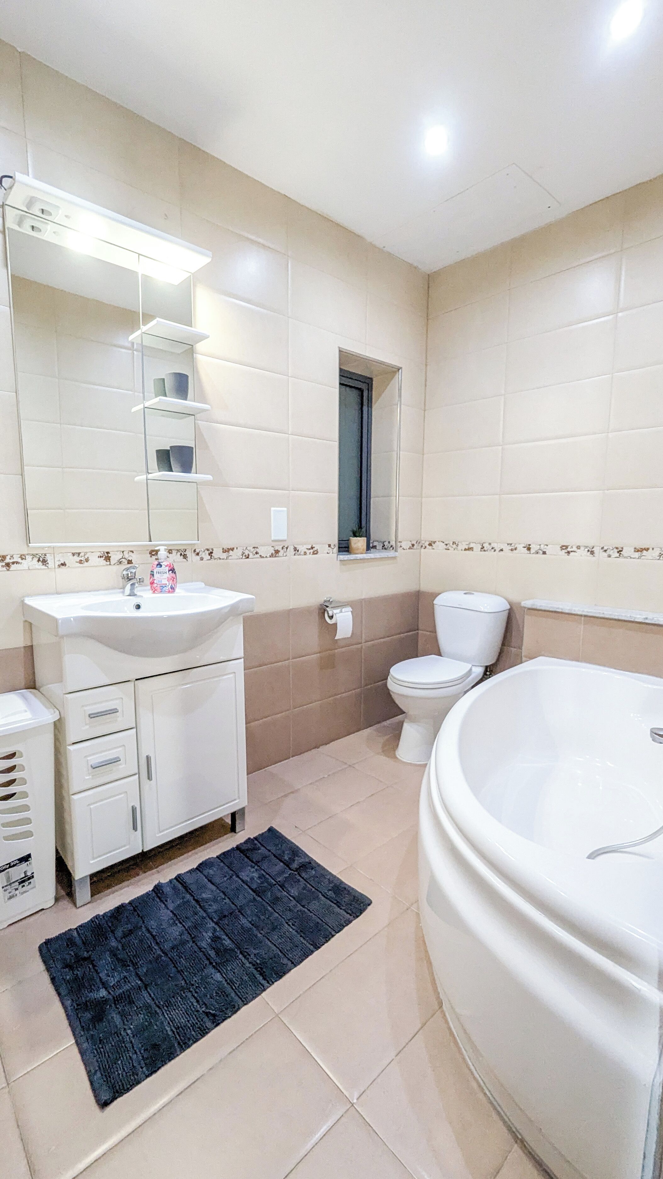A modern bathroom with a large bathtub, a sink with a mirror, a toilet, and a small shelf with decorative items.