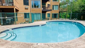 A swimming pool with a concrete deck, surrounded by a fence and a wooden building with balconies. - Lakeview At The Lodge Two Bedroom Suite (Two Harbors)