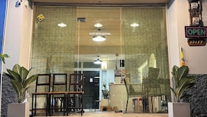 Der Eingang eines Hostels mit Glasfassade, einem Schild, das auf geöffneten Zustand hinweist, und einigen Stühlen draußen.