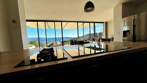 A modern kitchen with a large island, a view of the outdoors, and a dining area with chairs and a table. - Exceptional villa with panoramic view and heated pool (Sampzon)