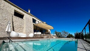 A swimming pool with stone walls, a covered patio, and outdoor seating. - Exceptional villa with panoramic view and heated pool (Sampzon)