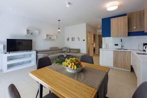 Una sala moderna con televisor, sofá y mesa de comedor con fruta.
