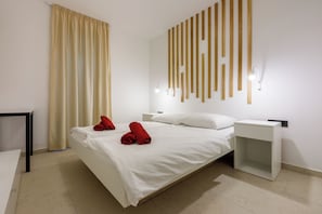 Una habitación de hotel moderna con una cama grande, una mesita de noche y una lámpara fijada en la pared.