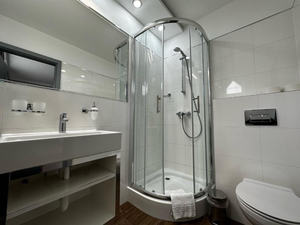 Un baño moderno con cabina de ducha de vidrio, lavabo blanco y retrete.