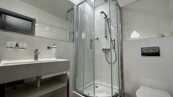 Un baño moderno con cabina de ducha de vidrio, lavabo blanco y retrete.