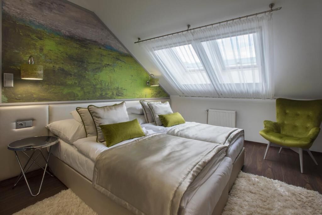 A bedroom with two beds, a green armchair, a small round table, and a large abstract painting on the wall.