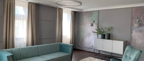 Ein modernes Wohnzimmer mit einem türkisfarbenen Sofa, einem Glastisch und einer weißen Kommode mit Pflanzen.