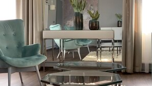 A modern living room with a teal armchair, a glass coffee table, and a dining area with a white table and chairs. - Boutique Hotel Center (Kecskemét)