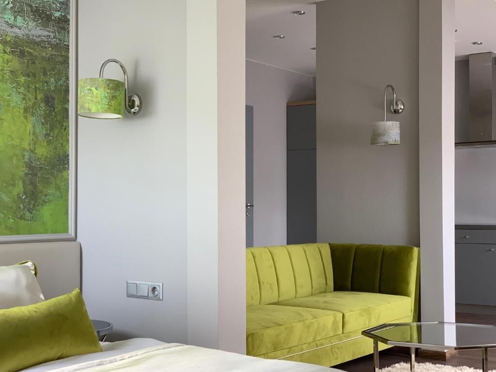 Une chambre d’hôtel moderne avec un canapé vert, une table basse en verre et une vue sur un paysage verdoyant par la fenêtre.