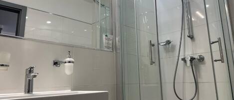 A modern bathroom with a glass-enclosed shower, a white sink with a chrome faucet, and a mirrored wall.