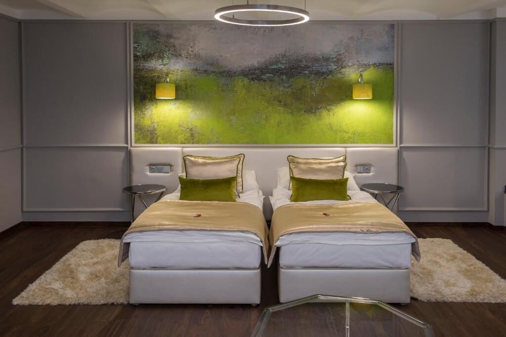 Un dormitorio moderno con dos camas, un cuadro abstracto grande y dos luces fijadas a la pared.