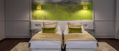 Un dormitorio moderno con dos camas, un cuadro abstracto grande y dos luces fijadas a la pared.