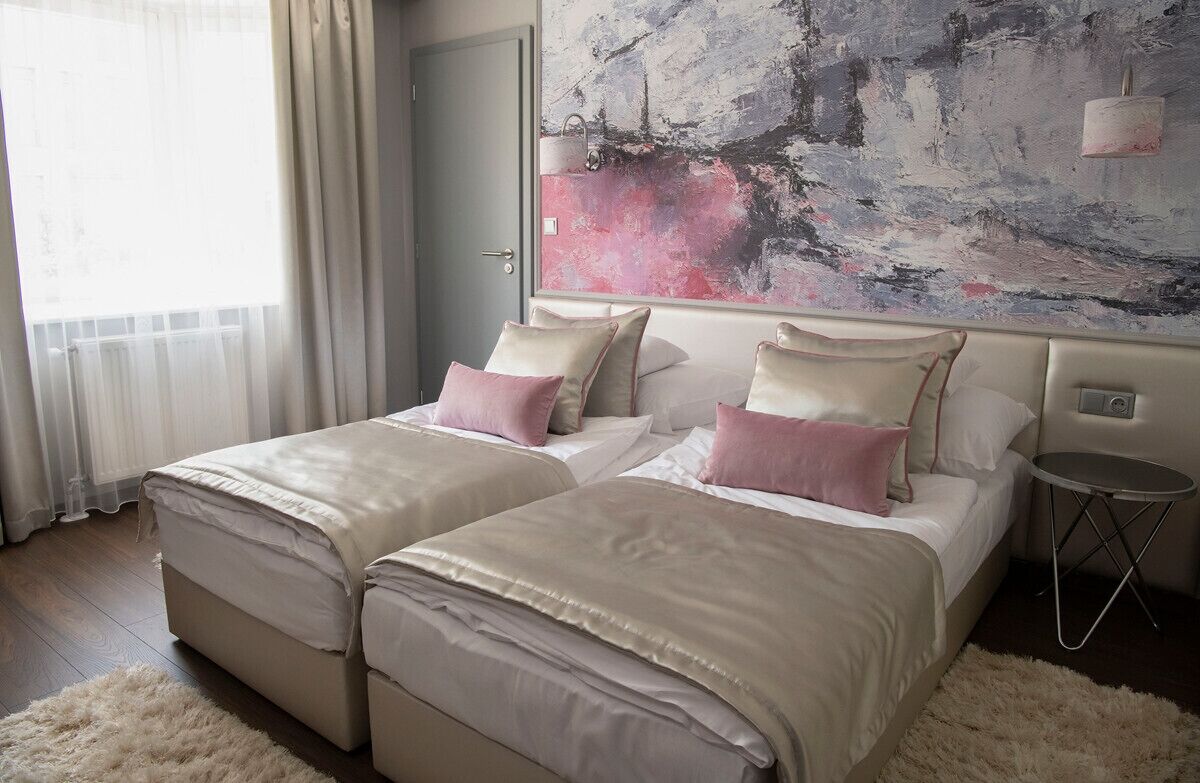 Habitación de hotel con dos camas, un cuadro abstracto grande en la pared, una mesita redonda pequeña y una alfombra mullida.