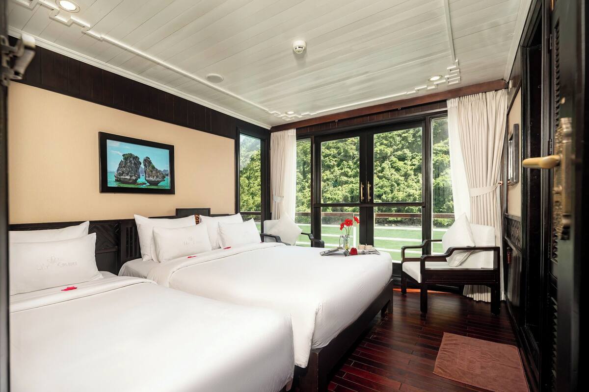 A hotel room with two beds, a large window with curtains, a chair, and a painting on the wall.