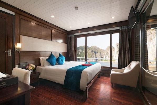 A hotel room with a large bed, a desk, a chair, and a view of the outdoors. - Halong Deluxe 1 Cruise (Tuan Chau)