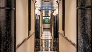 A corridor with a patterned floor, walls with a marble-like finish, and a ceiling with recessed lighting.