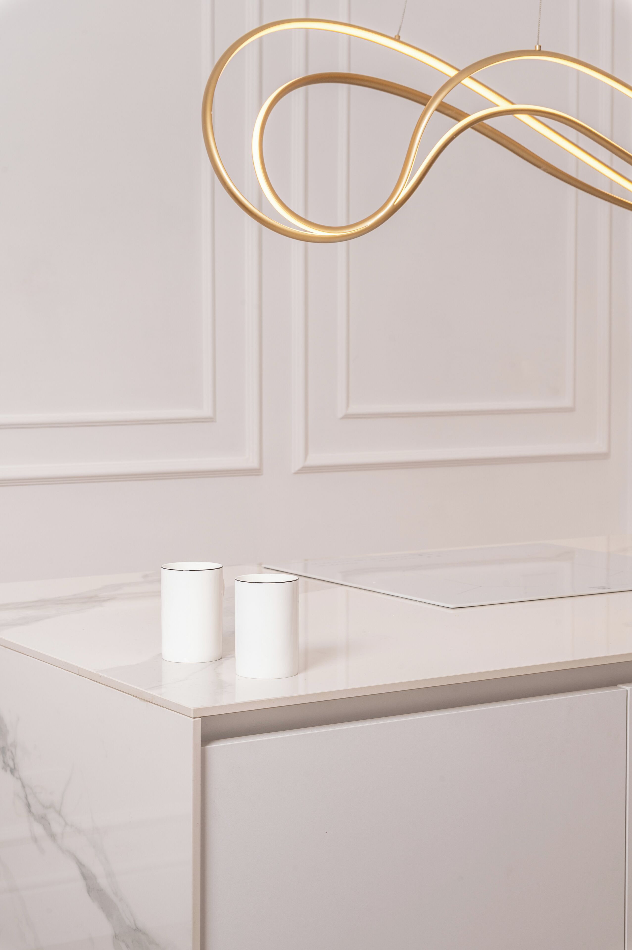 A modern bathroom with a marble countertop, two white cylindrical containers, and a gold-colored light fixture.
