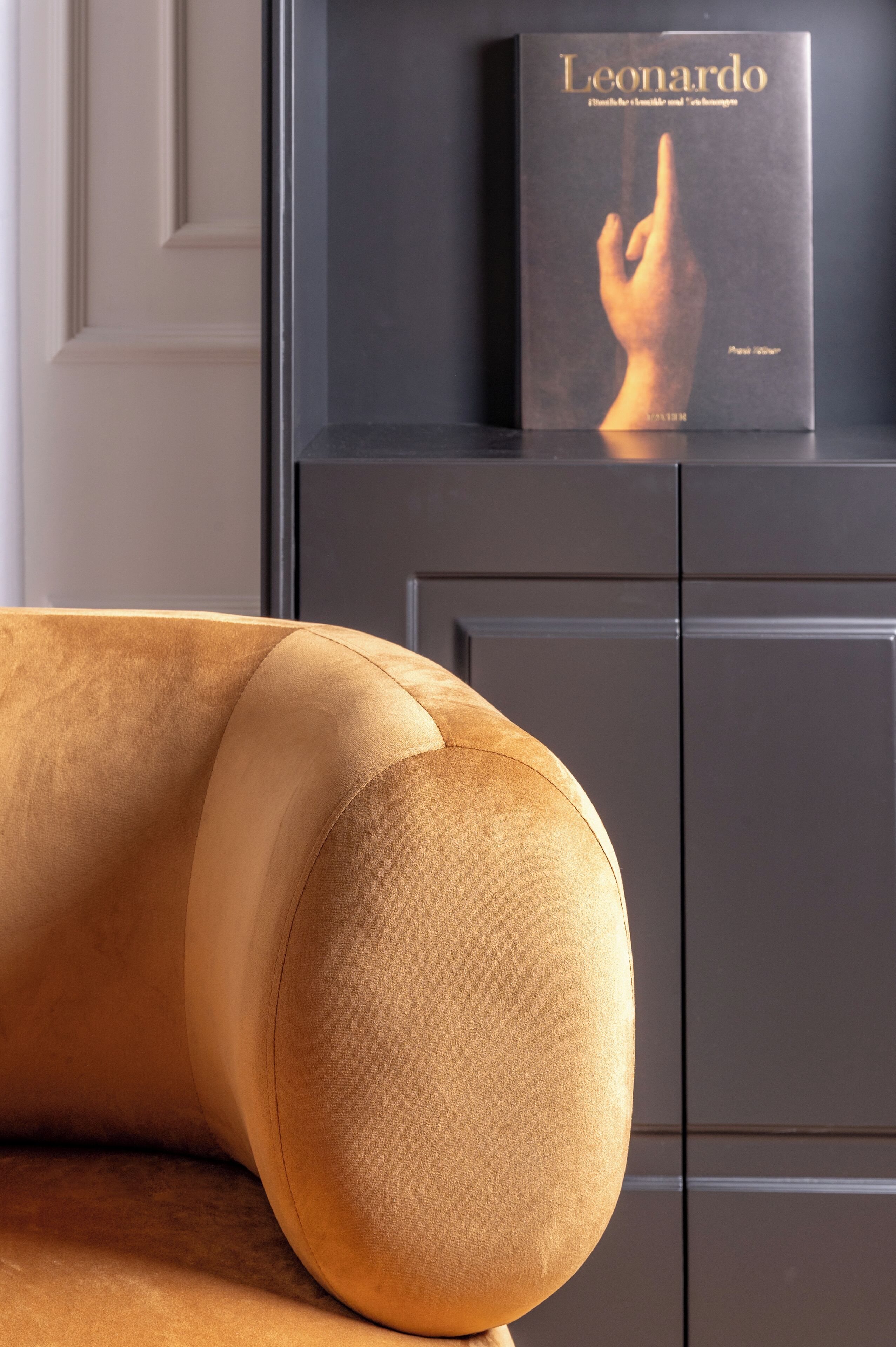 A sofa with a rounded backrest and a book titled "Leonardo" on a black cabinet.