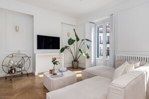 A modern living room with a sofa, a coffee table, a TV, and a large plant. - Waou Malasaña Luxe - Short-Term Rentals (Madrid)