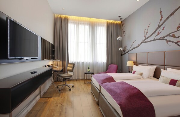 A hotel room with a TV, two beds, a desk, a chair, a small table, and a lamp. - Hotel Berlin Potsdamer Platz by Leonardo Hotels (Berlin)