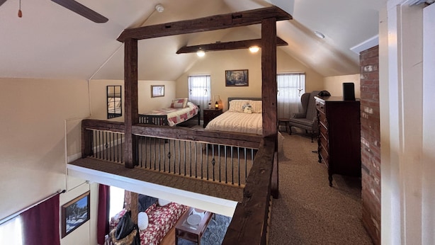 A bedroom with a sloped ceiling, a wooden ceiling fan, a bed with a quilt, a chair, and a dresser.
