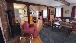 A spacious living area with a fireplace, a sofa, a plaid armchair, and a coffee table. A kitchen is visible in the background.