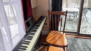 A piano near a window with curtains, a chair, and a lamp.