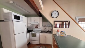 A compact kitchen with white appliances, a wooden floor, and a clock on the wall.