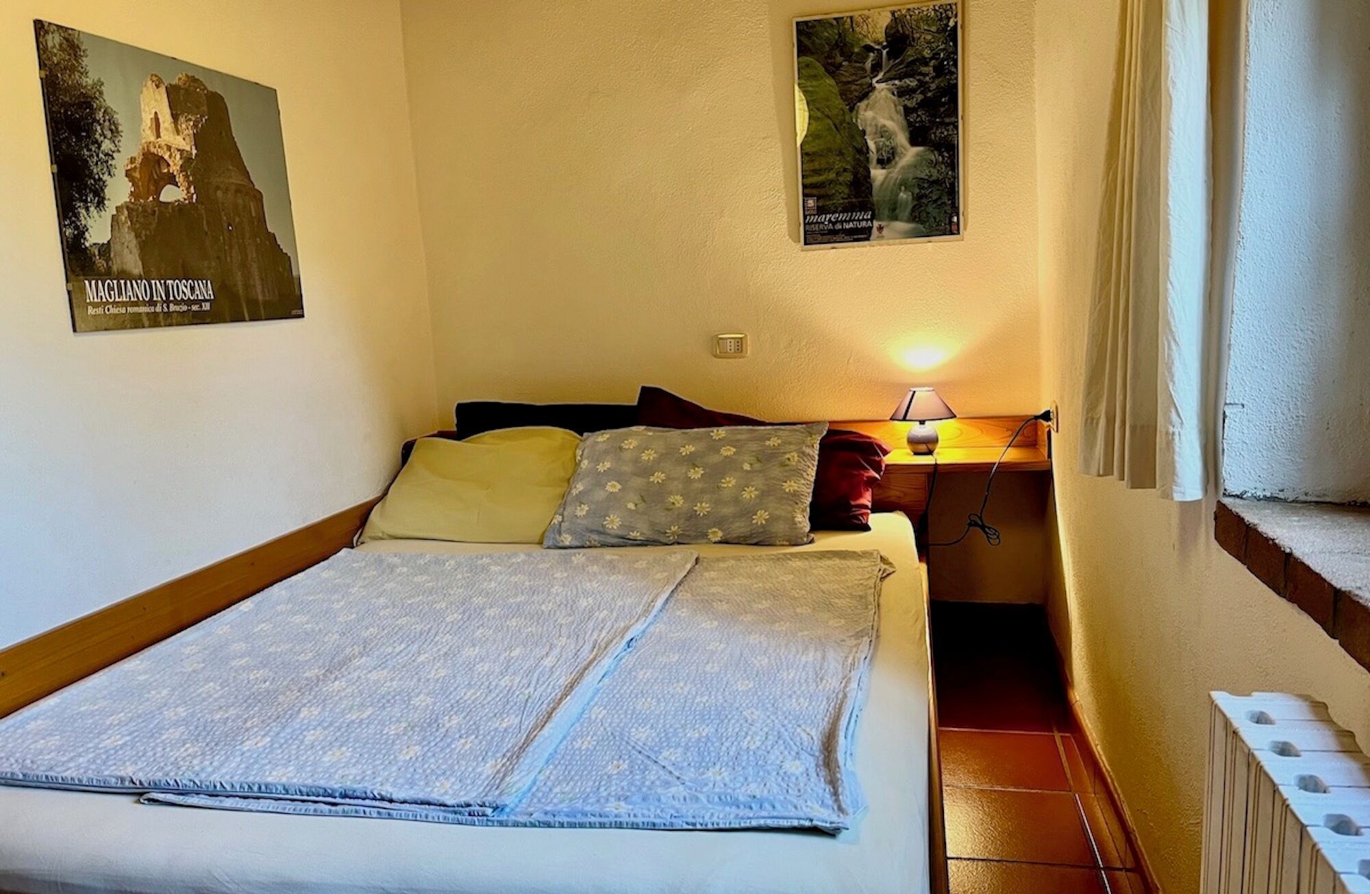 Ein Schlafzimmer mit Bett, Kissen, einem Nachttisch mit Lampe und zwei Bildern an der Wand.