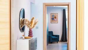 A hallway with a mirror, a vase with dried flowers, a framed picture on the wall, and a teal chair. - Villa Delphi (Swieqi)