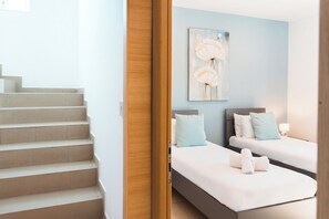 A hotel room with a staircase, two beds with pillows, a painting on the wall, and a wooden door. - Villa Delphi (Swieqi)