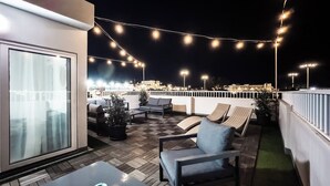 A rooftop terrace with outdoor seating, string lights, and a view of the cityscape at night. - Villa Delphi (Swieqi)