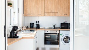 A modern kitchen with wooden cabinets, a coffee machine, a microwave, an oven, and a washing machine. - Villa Delphi (Swieqi)