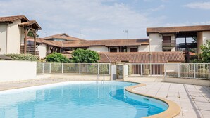 A swimming pool with a curved edge, surrounded by a white fence and buildings with tiled roofs.