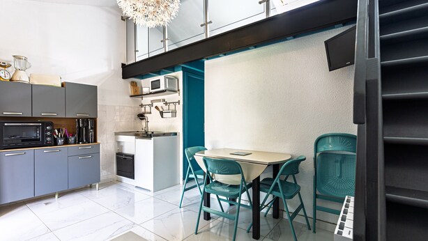 A modern kitchen with grey cabinets, a microwave, and a dining area with teal chairs and a table.