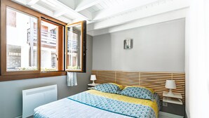 A bedroom with a bed, window, radiator, bedside table, and wall-mounted lamp.