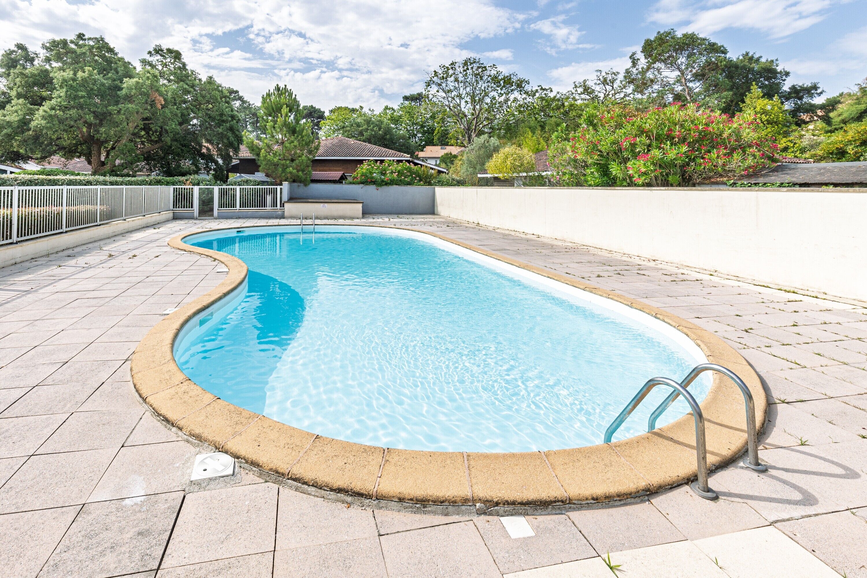 A swimming pool with a curved edge, surrounded by a white fence, and a paved walkway.