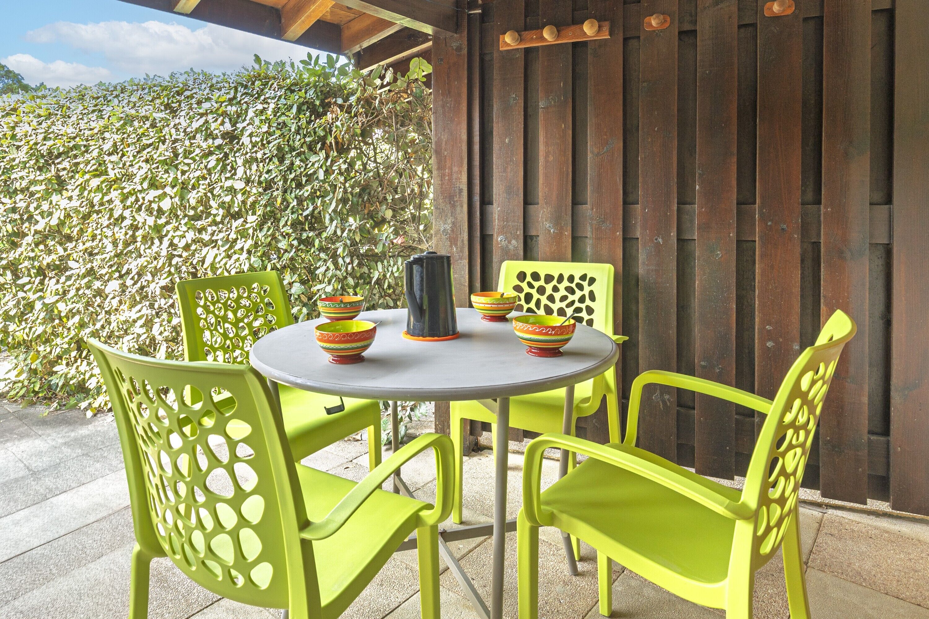 Een ronde tafel met vier stoelen, elk met een uniek uitgesneden ontwerp, buiten geplaatst met een houten hek en beplanting op de achtergrond.