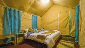 A tent-style room with a bed, pillows, a small table, and a rug. - Baspa Valley Adventure Camp (Rakchham)