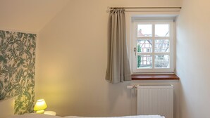 A bedroom with a bed, a nightstand with a lamp, a window with curtains, and a radiator. - Vacation apartment Göttingen - modern apartments near the hospital & university (Göttingen)