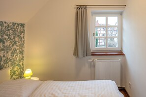 Ein Schlafzimmer mit einem Bett, einem Nachttisch mit Lampe, einem Fenster mit Vorhängen und einer Heizung.