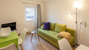 A modern living room with a green sofa, white chairs, a glass table, and a TV. - Vacation apartment Göttingen - modern apartments near the hospital & university (Göttingen)