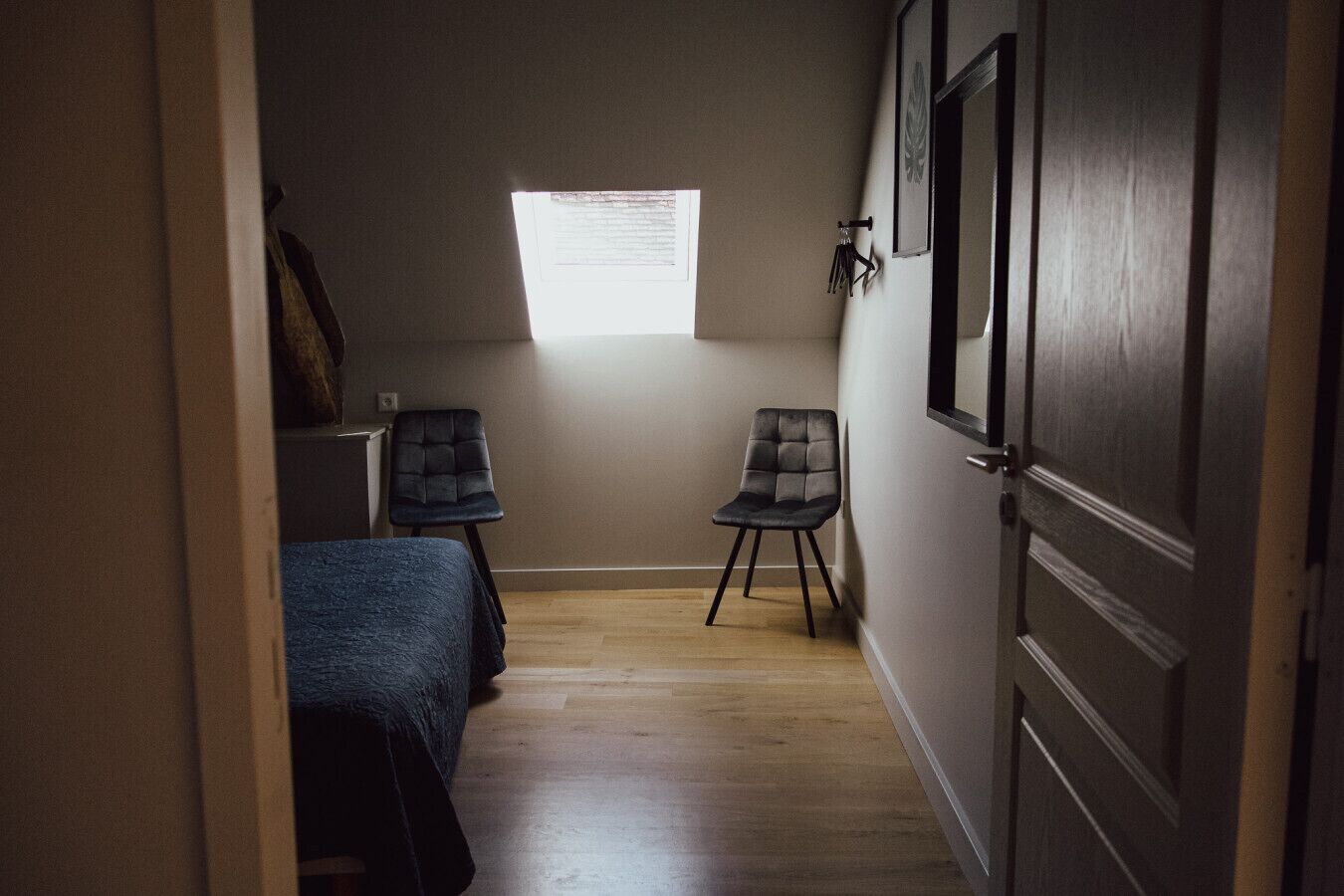 Une petite pièce comprenant un lit, deux chaises, une fenêtre et une porte.