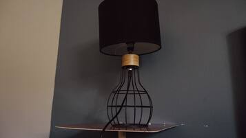 En moderne gulvlampe med skærm i sort og træsokkel, placeret på et lille bord foran en mørk væg.